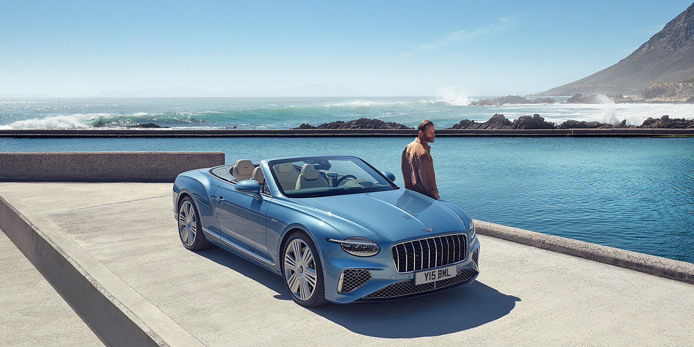 Bentley Copenhagen New Bentley Continental GTC Azure convertible front view in Light Windsor blue paint with 22 inch ten spoke wheels parked by the sea in the sunshine