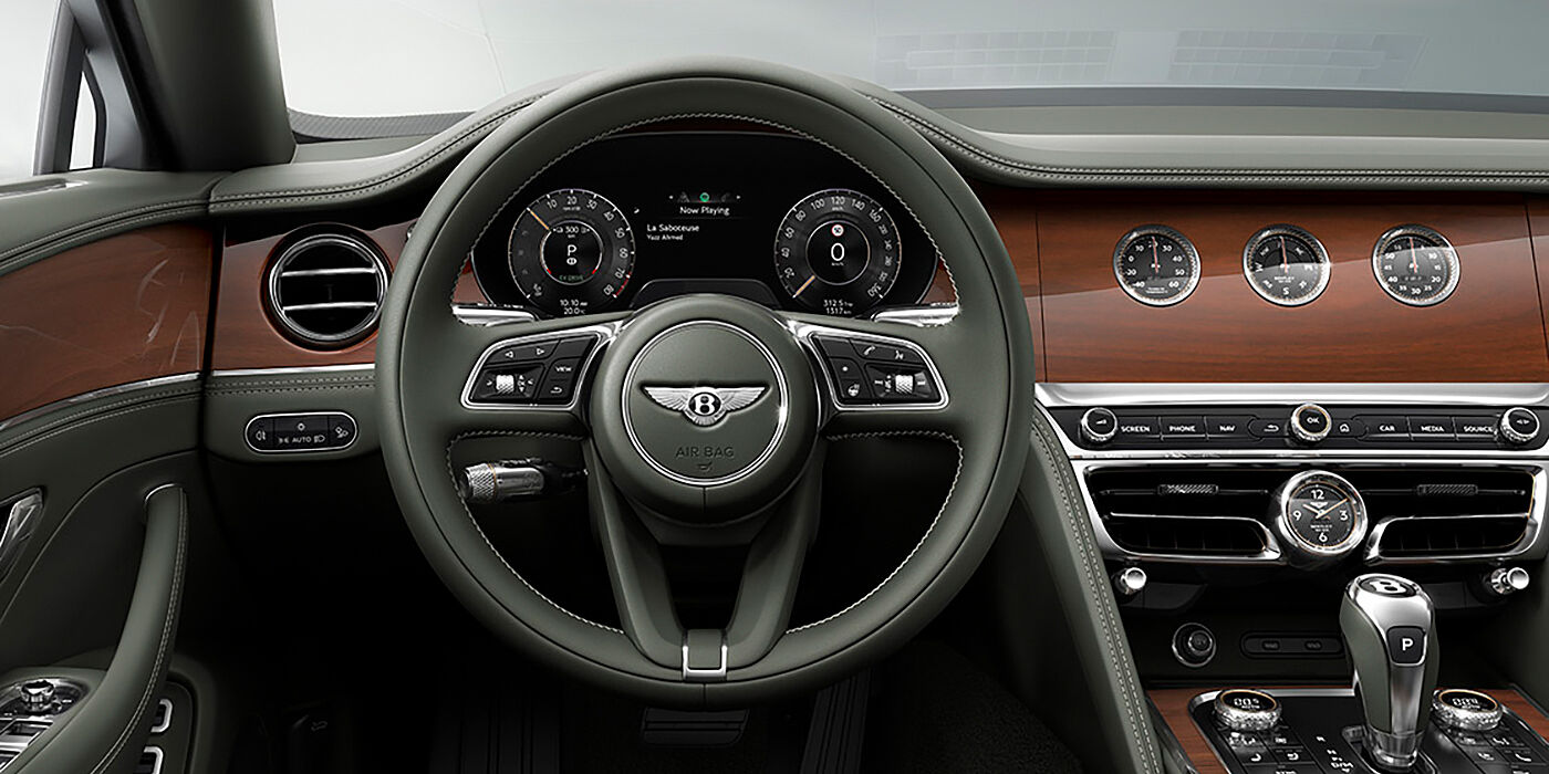 Bentley Copenhagen New Bentley Flying Spur sedan front cabin in Cumbrian Green hide and Crown Cut walnut veneer showing steering wheel and Rotating Display with three clocks on face