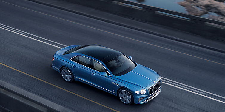 Bentley Copenhagen New Bentley Flying Spur Azure sedan in Light windsor blue paint by Mulliner, with 22 inch Azure wheels seen from overhead driving dynamically on a country road