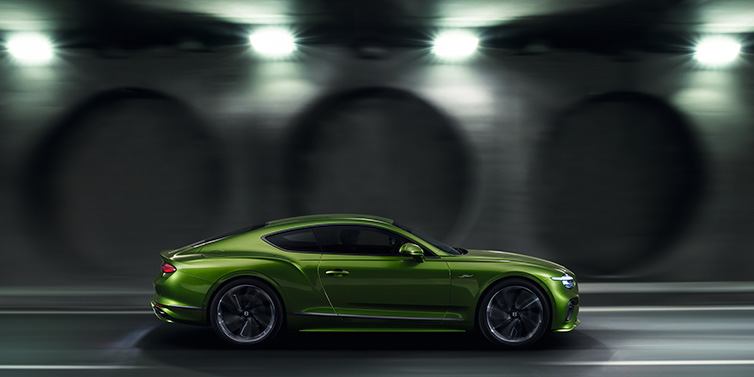 Bentley Copenhagen Bentley Continental GT Speed coupe profile in Tourmaline Green driving dynamically past a concrete wall at night