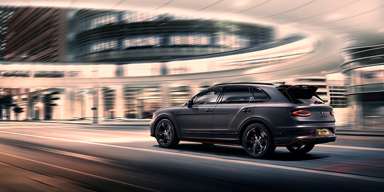 Bentley Copenhagen Bentley Bentayga S Black Edition SUV rear three quarter in Anthracite Satin paint driving dynamically through a city at night