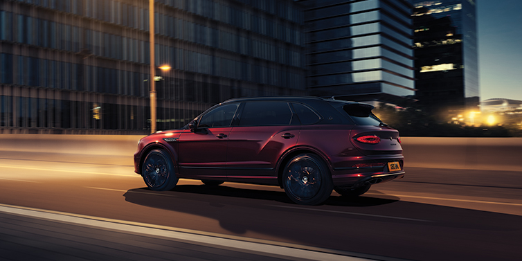 Bentley Copenhagen Bentley Bentayga Extended Wheelbase Mulliner SUV in Cricket Ball red paint driving dynamically in city at night