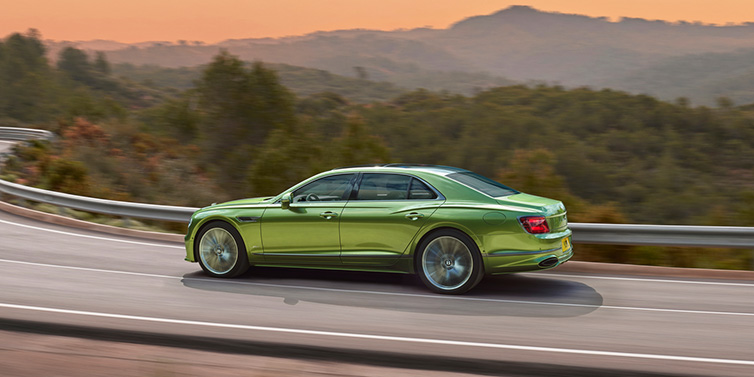 Bentley Copenhagen Bentley Flying Spur Speed sedan side profile in Tourmaline Green paint driving dynamically on a mountain road at sunset